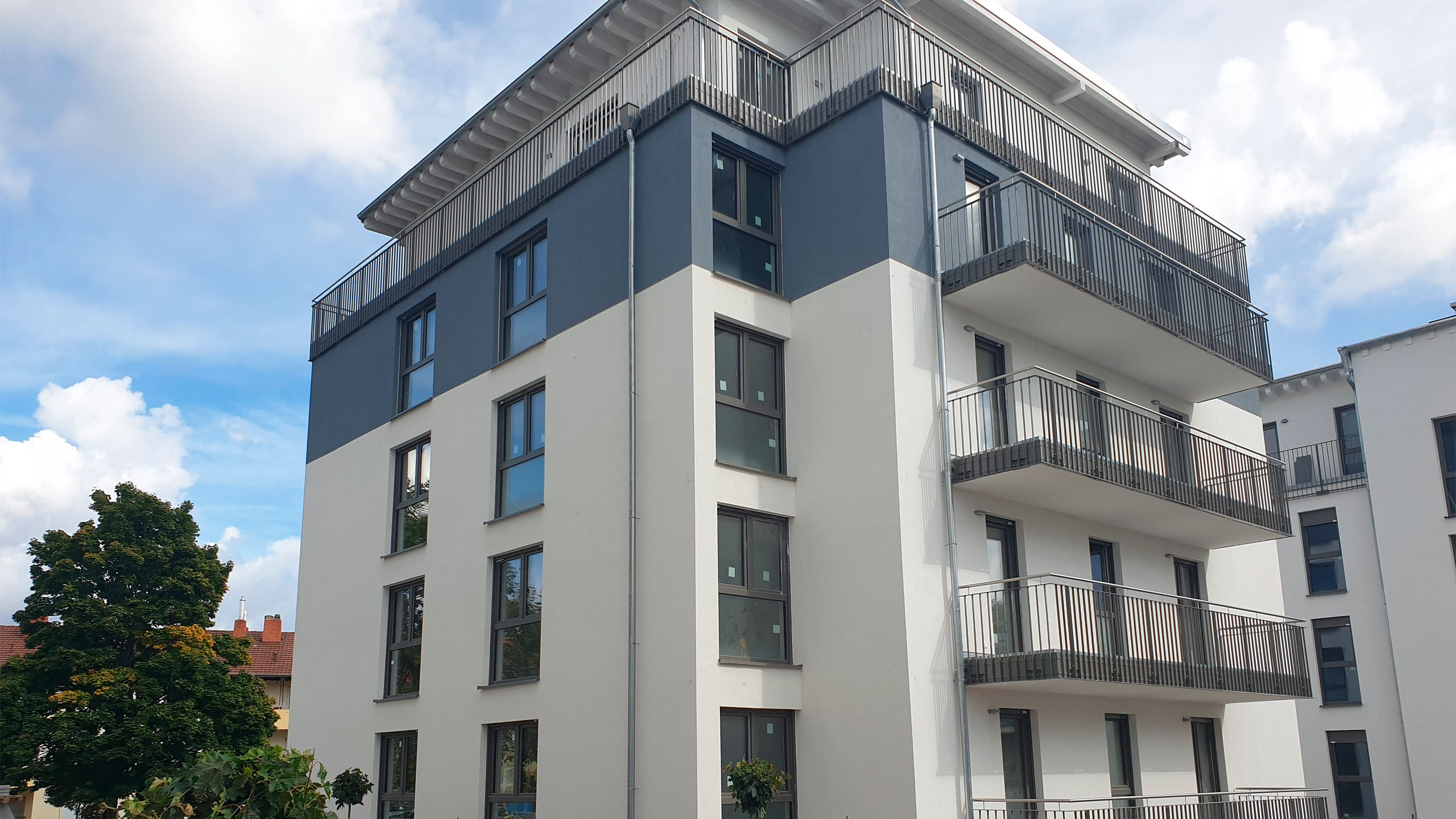 Ein modernes Mehrfamilienhaus mit grau-weißer Fassade und umlaufenden Balkonen.