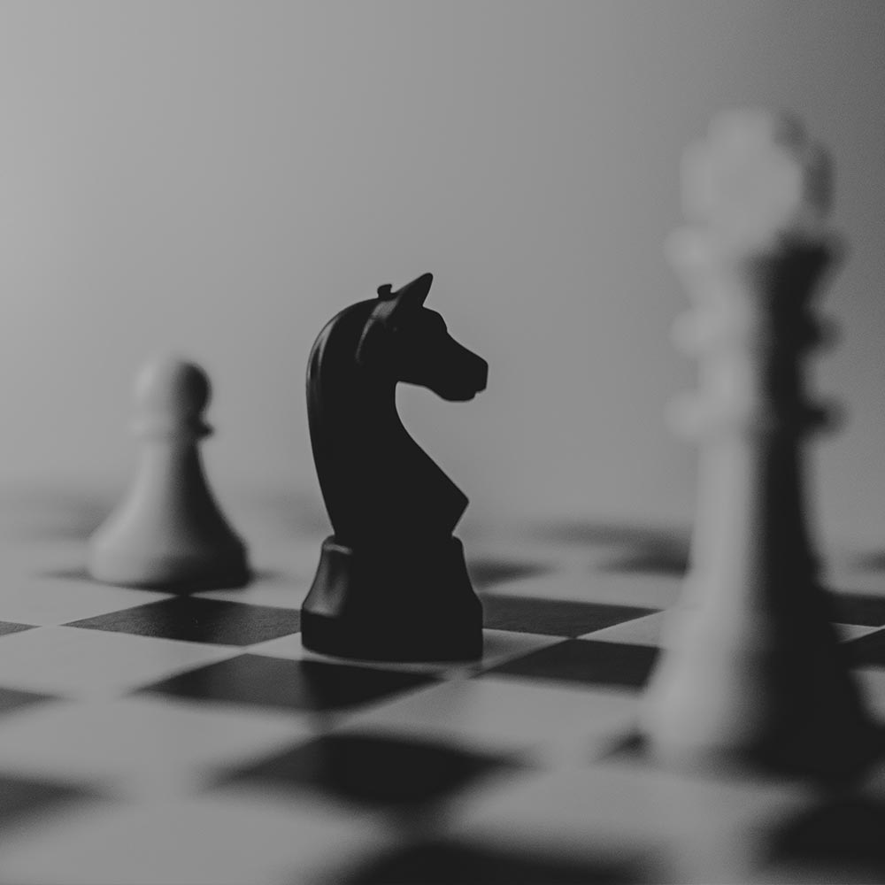 Ein schwarzer Springer steht auf einem Schachbrett zwischen weißen Figuren.